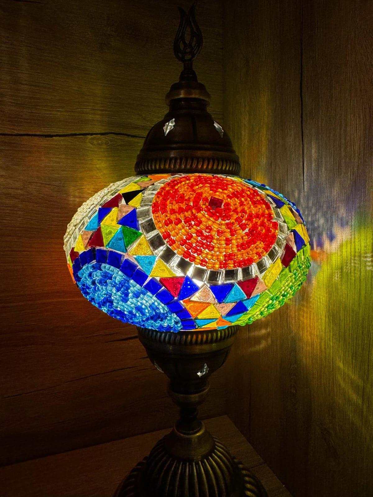 Two-tone red and blue mosaic lamp casting jewel-toned light onto the wooden wall