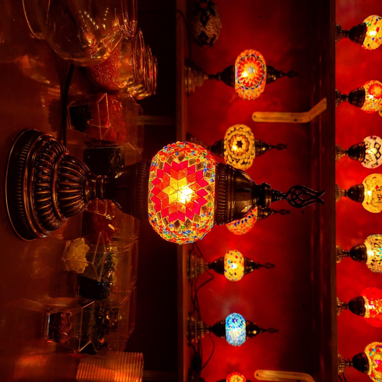 A red star-pattern mosaic lamp on the workbench, shelves of glowing lamps behind