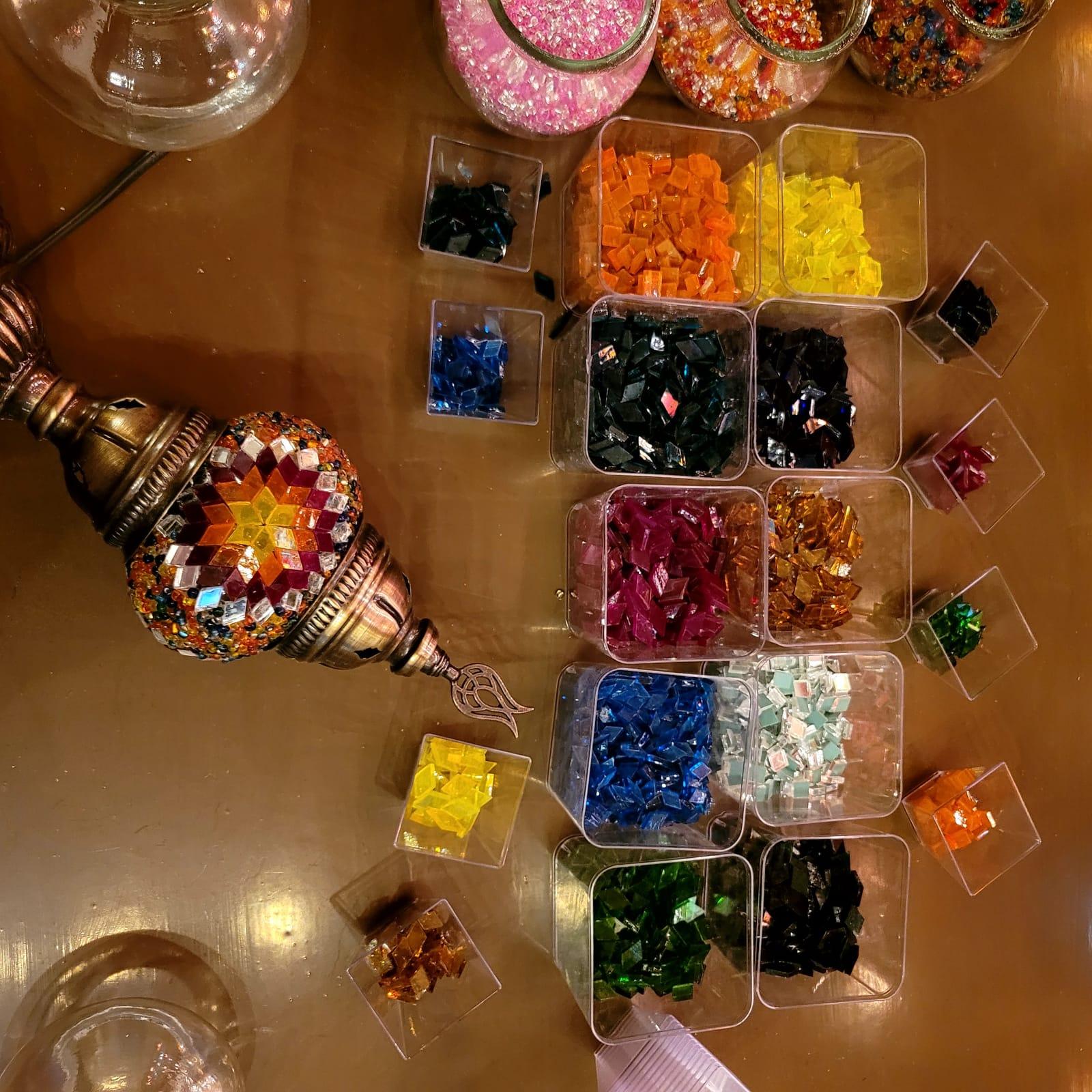 Overhead view of the workshop table with glass tesserae spread out and a lamp in progress